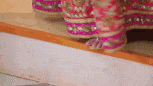 a woman in a pink and gold dress is standing on a wooden ledge