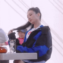 a woman in a blue and black jacket is sitting at a table with a hourglass .