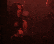 a man with long hair is singing into a microphone in the dark