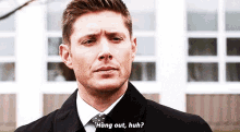 a man in a suit and tie is standing in front of a building and says `` hang out , huh ? ''