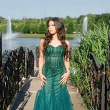 a woman in a green dress stands on a bridge over a lake