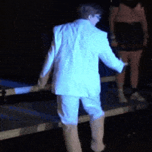 a man in a white suit is dancing on a stage in front of a blue light .