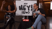 a man and woman are sitting in front of a sign that says hey