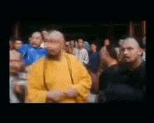 a man in a yellow robe is standing in front of a crowd of people in a room .