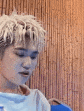 a man with blonde hair is sitting in front of a bamboo wall