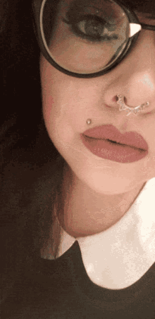 a close up of a woman 's face with a nose ring and glasses