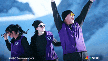 a man in a purple vest with the letter x on it stands in front of two other people