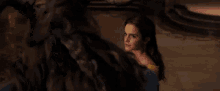a woman in a yellow dress is standing in front of a beast in a dark room .