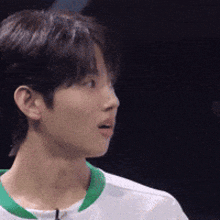 a young man wearing a white shirt with a green collar is looking away from the camera .