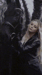 a woman in a black leather jacket stands next to a black horse