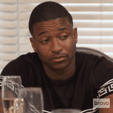a man sitting at a table with a glass of wine and a bravo logo on his shirt