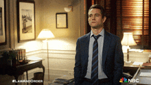 a man in a suit and tie is standing in a room with a nbc logo