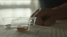 a person 's hand is reaching for a small cup of liquid on a table