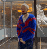 a man wearing a blue and red sweater stands in front of a broken glass window