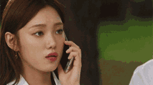 a woman is talking on a cell phone with a man in the background .