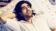 a man with long hair is laying on a bed with his hand behind his head