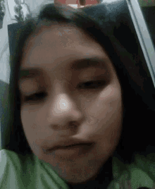 a close up of a girl 's face with her eyes closed and a green shirt on .