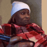 a woman wearing a white beanie and a plaid shirt is holding a remote control