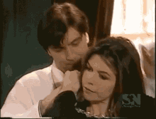 a man is touching a woman 's face with a sn logo on the bottom right