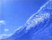 a blue sky with a few clouds and a wave in the foreground