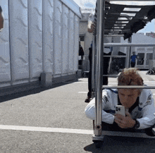 a man in a white shirt with the word racing on it looks down at his phone