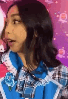a girl in a blue plaid dress with a blue flower on her collar is making a face .