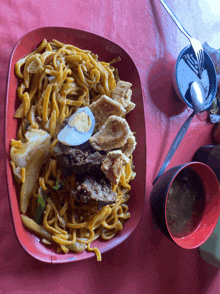 a plate of noodles with meat and eggs next to a bowl of soup