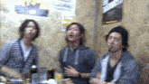 a blurry photo of three men sitting at a table with a poster on the wall that says ' tokyo '