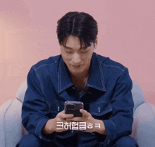 a man in a blue jacket is looking at his phone with a pink background