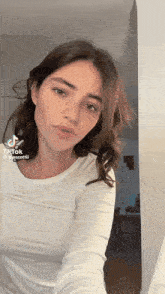 a woman in a white shirt is taking a selfie with a tiktok sticker