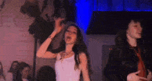 a woman in a white tank top is dancing with another woman in a dark room .