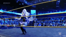 a woman is dancing in a wrestling ring while a referee stands behind her