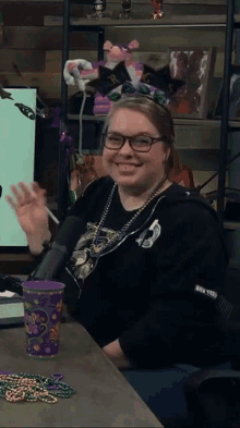 a woman sitting at a table with a microphone and a purple cup that says mardi gras on it