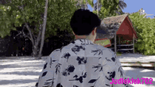 a man in a floral shirt is walking on a beach with the name judleklek702 on the bottom right