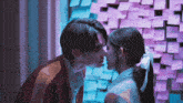 a boy and a girl kissing in front of a wall with sticky notes on it