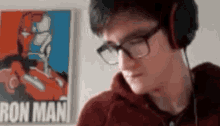 a man wearing headphones and glasses is looking at a poster of iron man .
