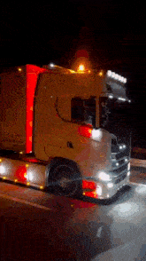 a yellow truck with a red stripe on the side is driving down a highway at night