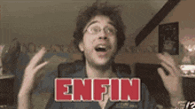 a man with glasses is making a funny face with the word enfin in red letters