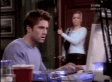 a man is sitting at a desk using a computer while a woman stands behind him