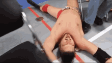 a shirtless wrestler is laying on the floor in a ring .