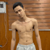 a young man without a shirt is standing in front of a window with blinds