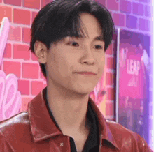 a close up of a young man wearing a red leather jacket and a black shirt .