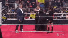 a man in a suit is standing in a wrestling ring with a woman .