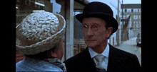 a man wearing a bowler hat and glasses is talking to a woman wearing a straw hat