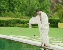 a man wrapped in a white towel stands on the edge of a swimming pool