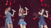 three women are dancing on stage with microphones in their hands .