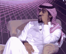 a man wearing a white shirt and a head scarf sits in a chair