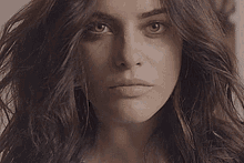 a woman with long brown hair is looking at the camera