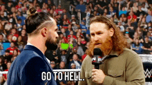 a man with a beard is talking to another man in a wrestling ring while holding a microphone .