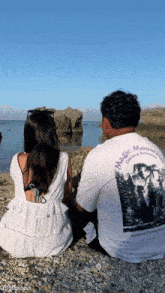 a man wearing a magic mountain shirt sits next to a woman on a beach